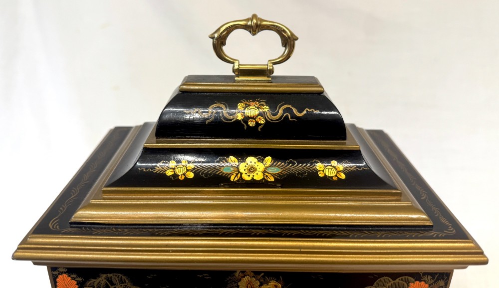 A black lacquered chinoiserie bracket clock featuring hand-painted gilt landscape scenes, a brass dial with Roman numerals, and a top brass carrying handle. View V