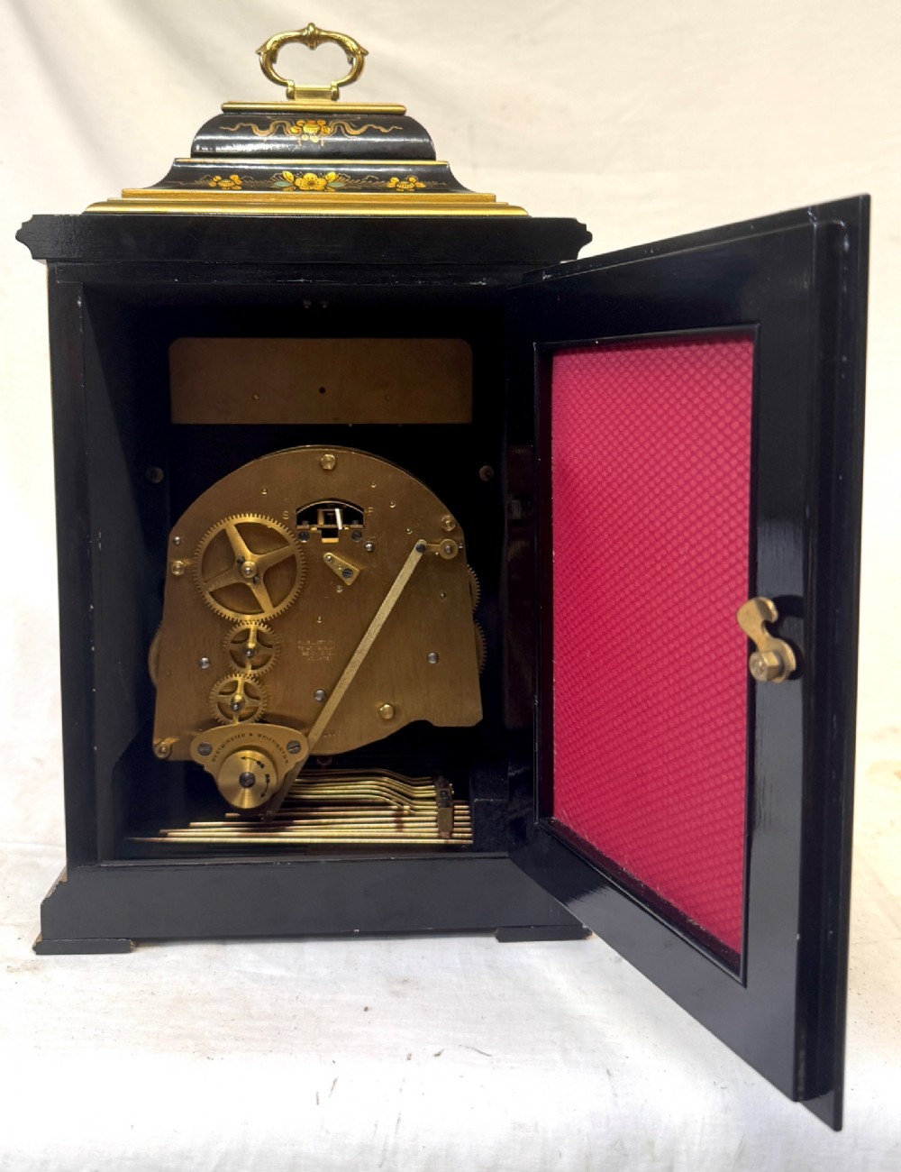 A black lacquered chinoiserie bracket clock featuring hand-painted gilt landscape scenes, a brass dial with Roman numerals, and a top brass carrying handle. View IX