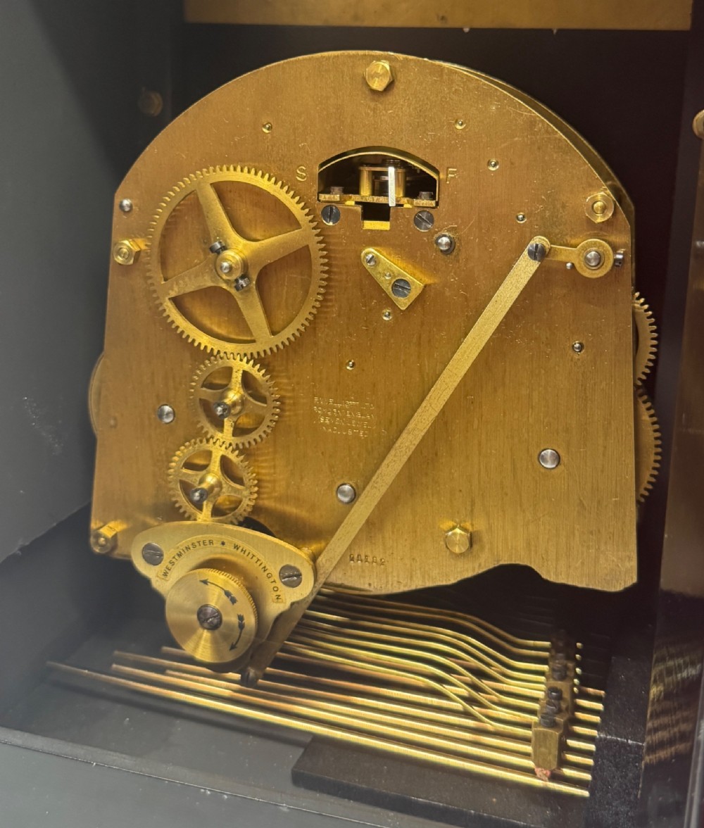 A black lacquered chinoiserie bracket clock featuring hand-painted gilt landscape scenes, a brass dial with Roman numerals, and a top brass carrying handle. View X