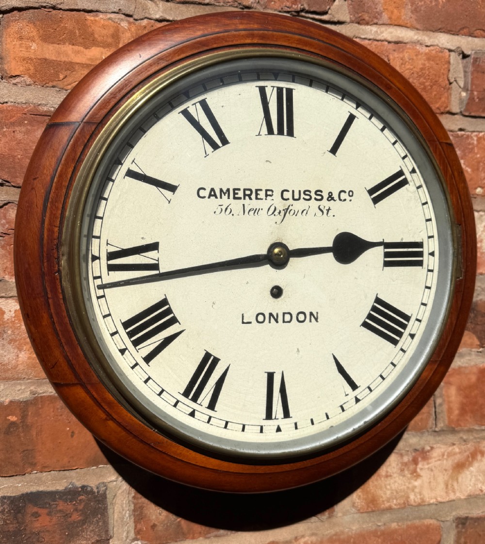 A circular Victorian mahogany wall clock with a cream painted dial displaying Roman numerals, makers inscription for Camerer Cuss & Co London, and a brass bezel.
