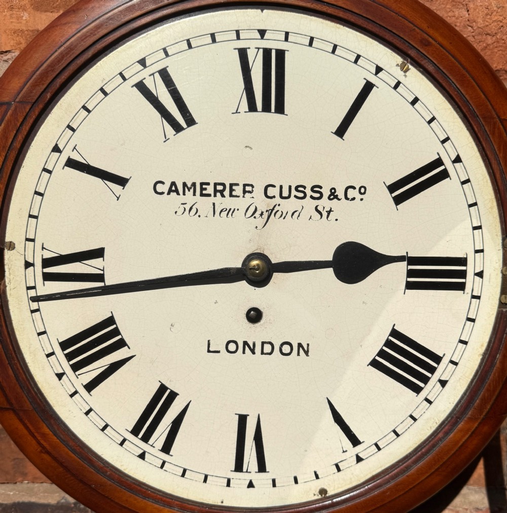 A circular Victorian mahogany wall clock with a cream painted dial displaying Roman numerals, makers inscription for Camerer Cuss & Co London, and a brass bezel. View IV