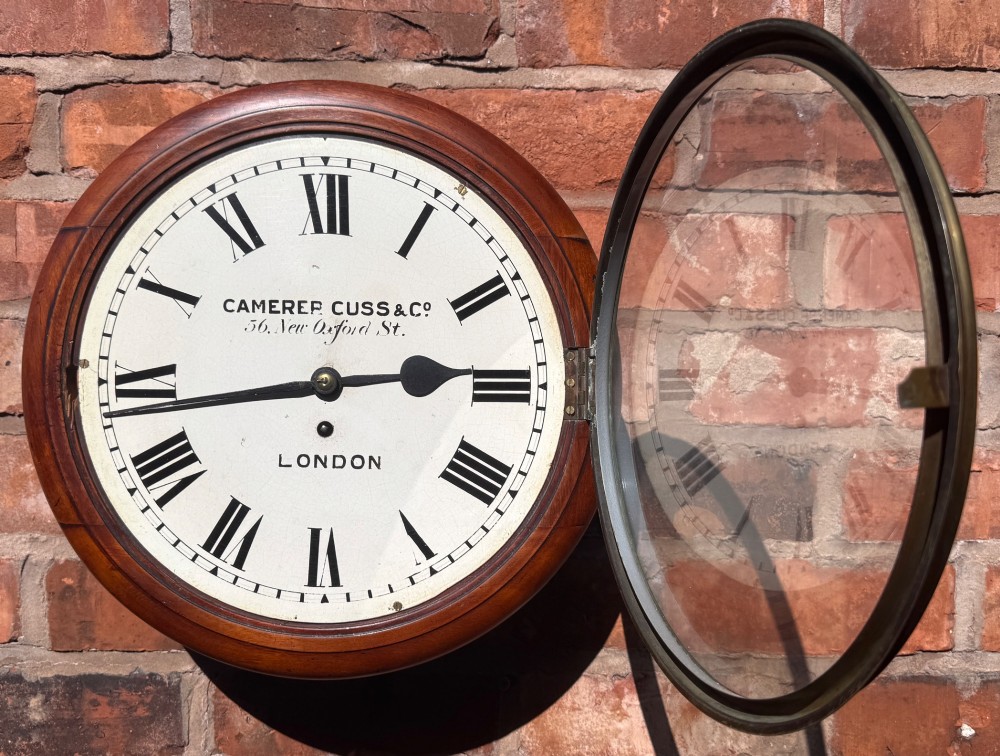 A circular Victorian mahogany wall clock with a cream painted dial displaying Roman numerals, makers inscription for Camerer Cuss & Co London, and a brass bezel. View VII