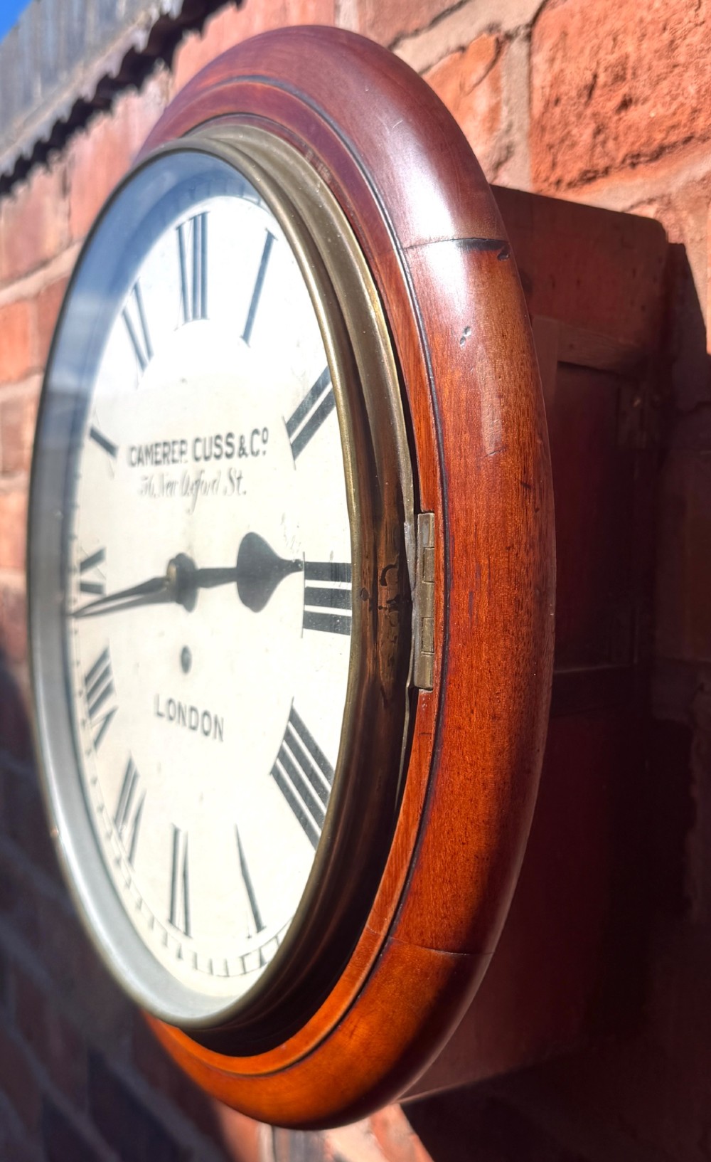 A circular Victorian mahogany wall clock with a cream painted dial displaying Roman numerals, makers inscription for Camerer Cuss & Co London, and a brass bezel. View VIII