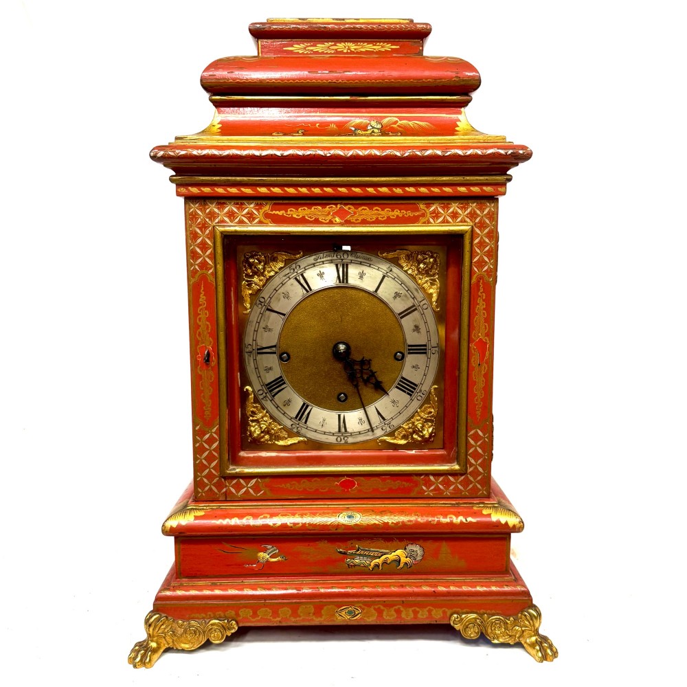 A red lacquered bracket clock decorated with gold chinoiserie motifs, featuring a brass dial and gilt metal feet. View II
