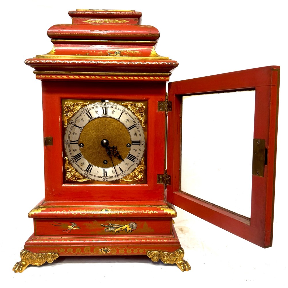 A red lacquered bracket clock decorated with gold chinoiserie motifs, featuring a brass dial and gilt metal feet. View III