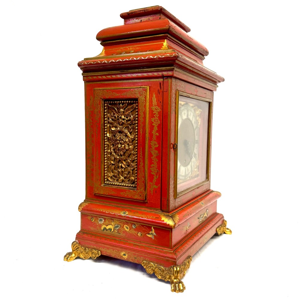 A red lacquered bracket clock decorated with gold chinoiserie motifs, featuring a brass dial and gilt metal feet. View IV