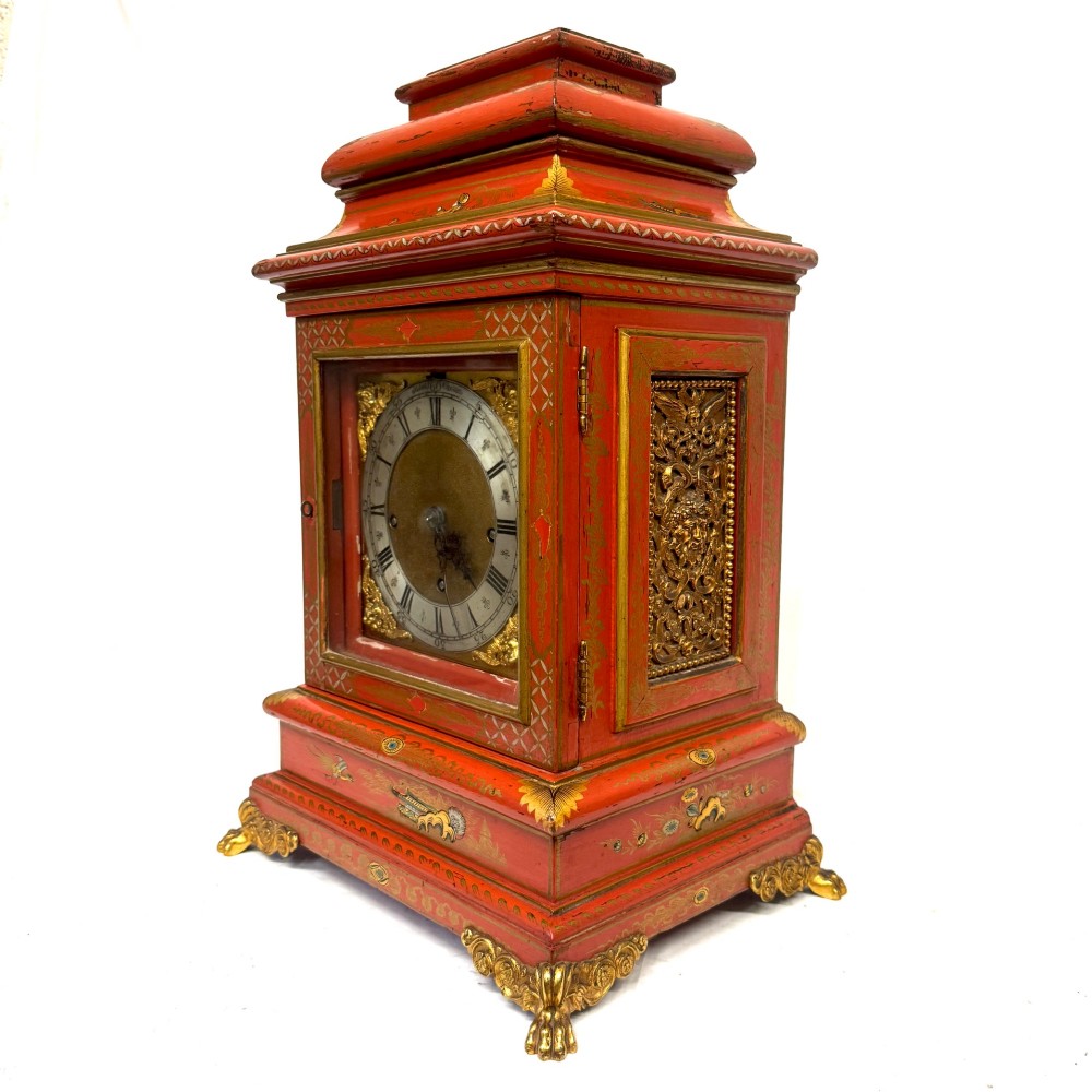 A red lacquered bracket clock decorated with gold chinoiserie motifs, featuring a brass dial and gilt metal feet. View VI