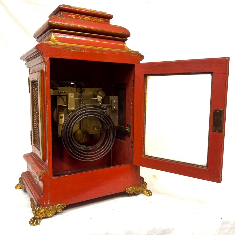A red lacquered bracket clock decorated with gold chinoiserie motifs, featuring a brass dial and gilt metal feet. View VII
