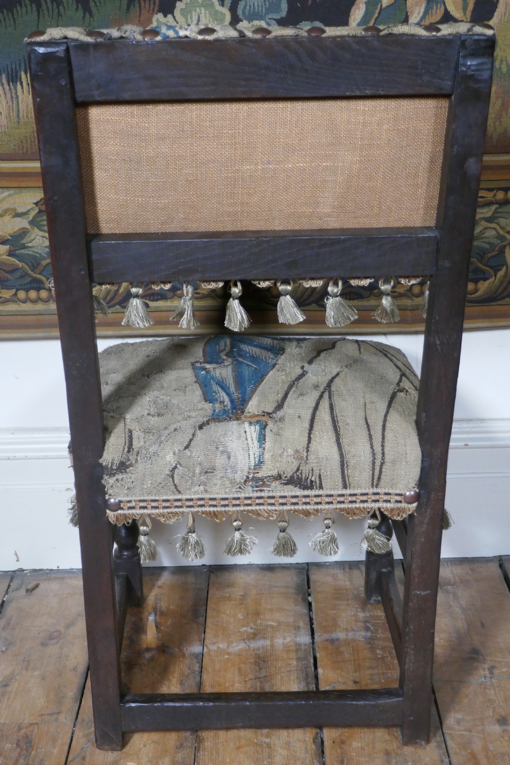 A pair of 17th-century oak back stools upholstered in tapestry fabric with tassel trim and turned legs. View V