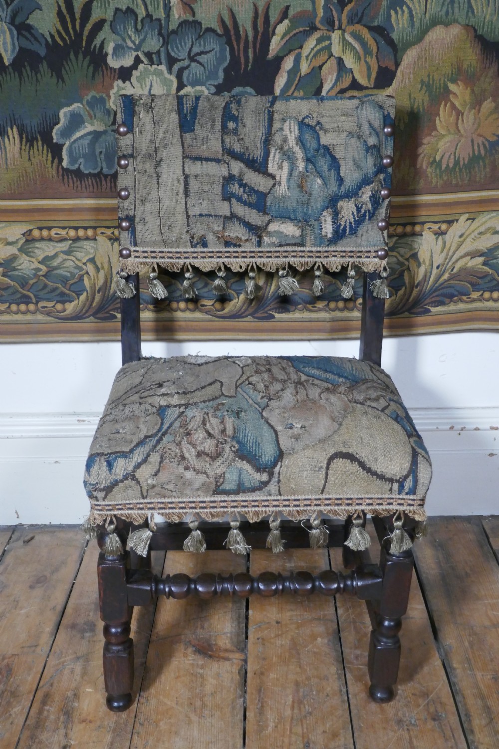 A pair of 17th-century oak back stools upholstered in tapestry fabric with tassel trim and turned legs. View VI