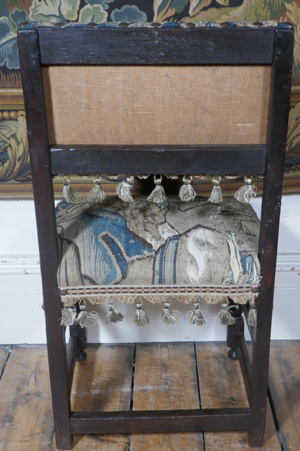 A pair of 17th-century oak back stools upholstered in tapestry fabric with tassel trim and turned legs. View X