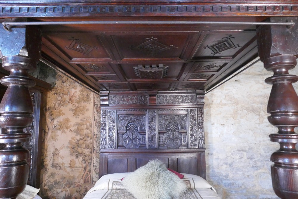 A dark oak 17th-century full tester bed featuring a relief-carved headboard, turned front posts, and a coffered ceiling canopy. View II