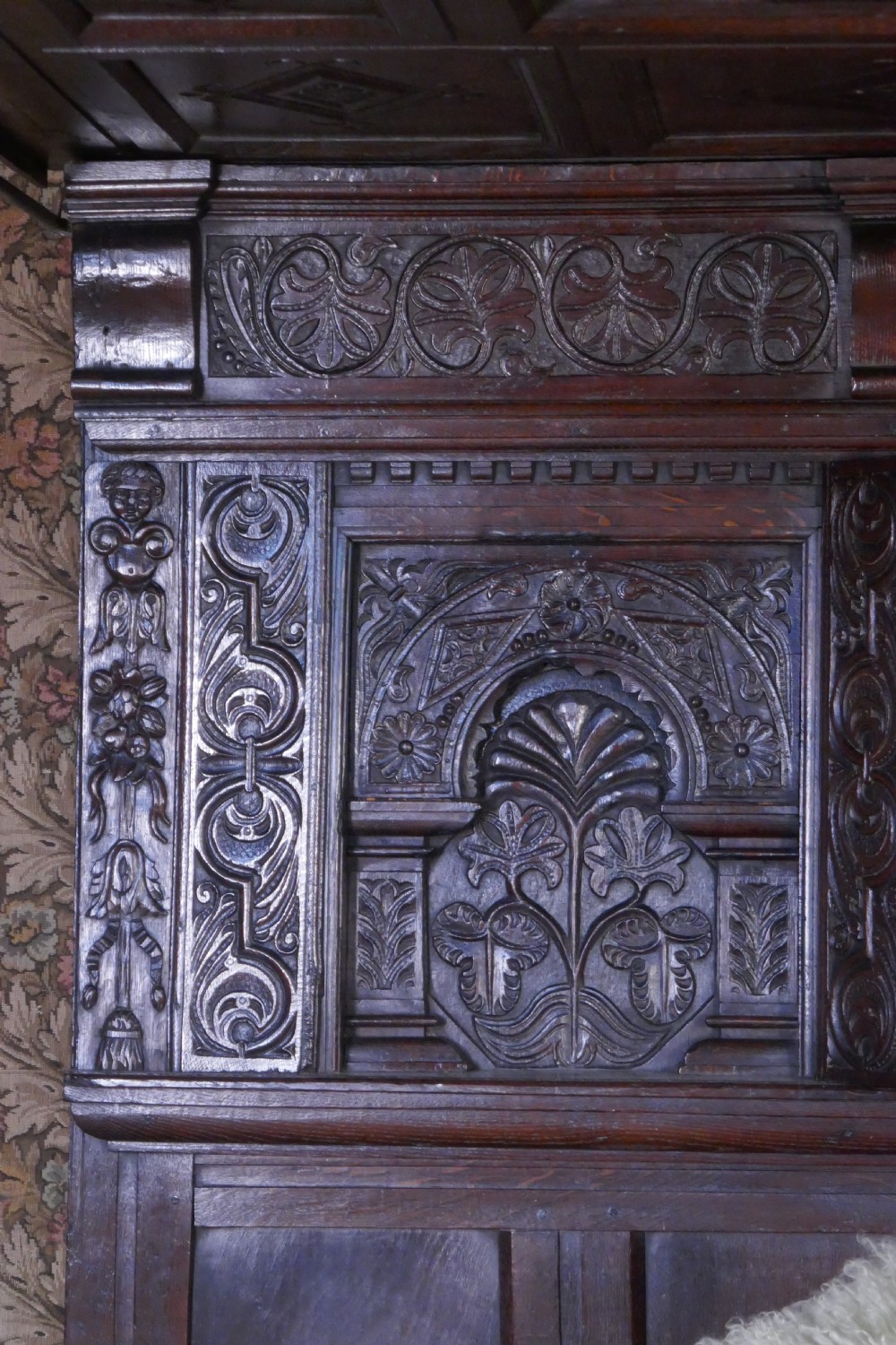 A dark oak 17th-century full tester bed featuring a relief-carved headboard, turned front posts, and a coffered ceiling canopy. View VII