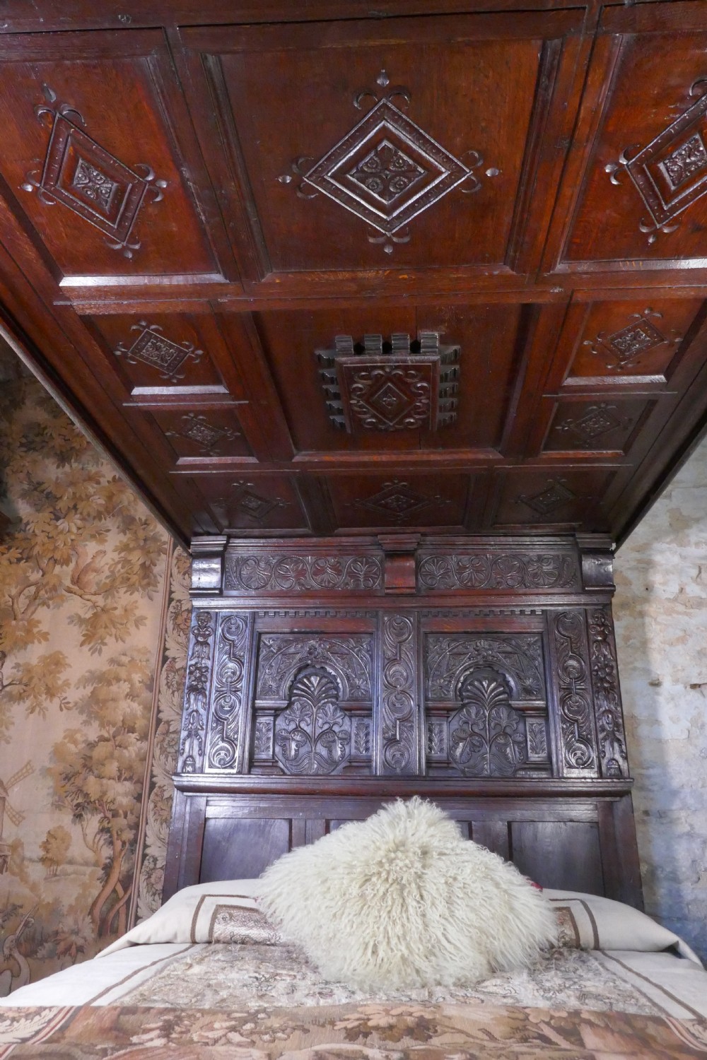 A dark oak 17th-century full tester bed featuring a relief-carved headboard, turned front posts, and a coffered ceiling canopy. View IX