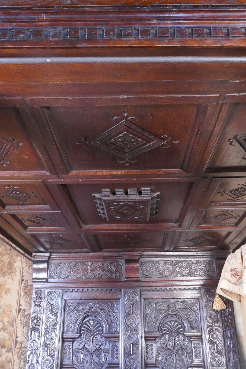 A dark oak 17th-century full tester bed featuring a relief-carved headboard, turned front posts, and a coffered ceiling canopy. View X