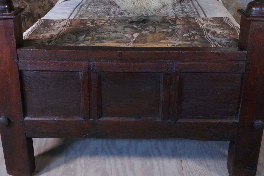 A dark oak 17th-century full tester bed featuring a relief-carved headboard, turned front posts, and a coffered ceiling canopy. View XV