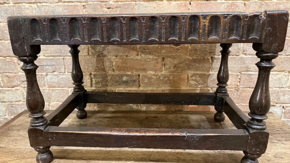 A dark oak 17th-century joint stool featuring a carved arcaded apron, turned legs, and lower box stretchers. View III