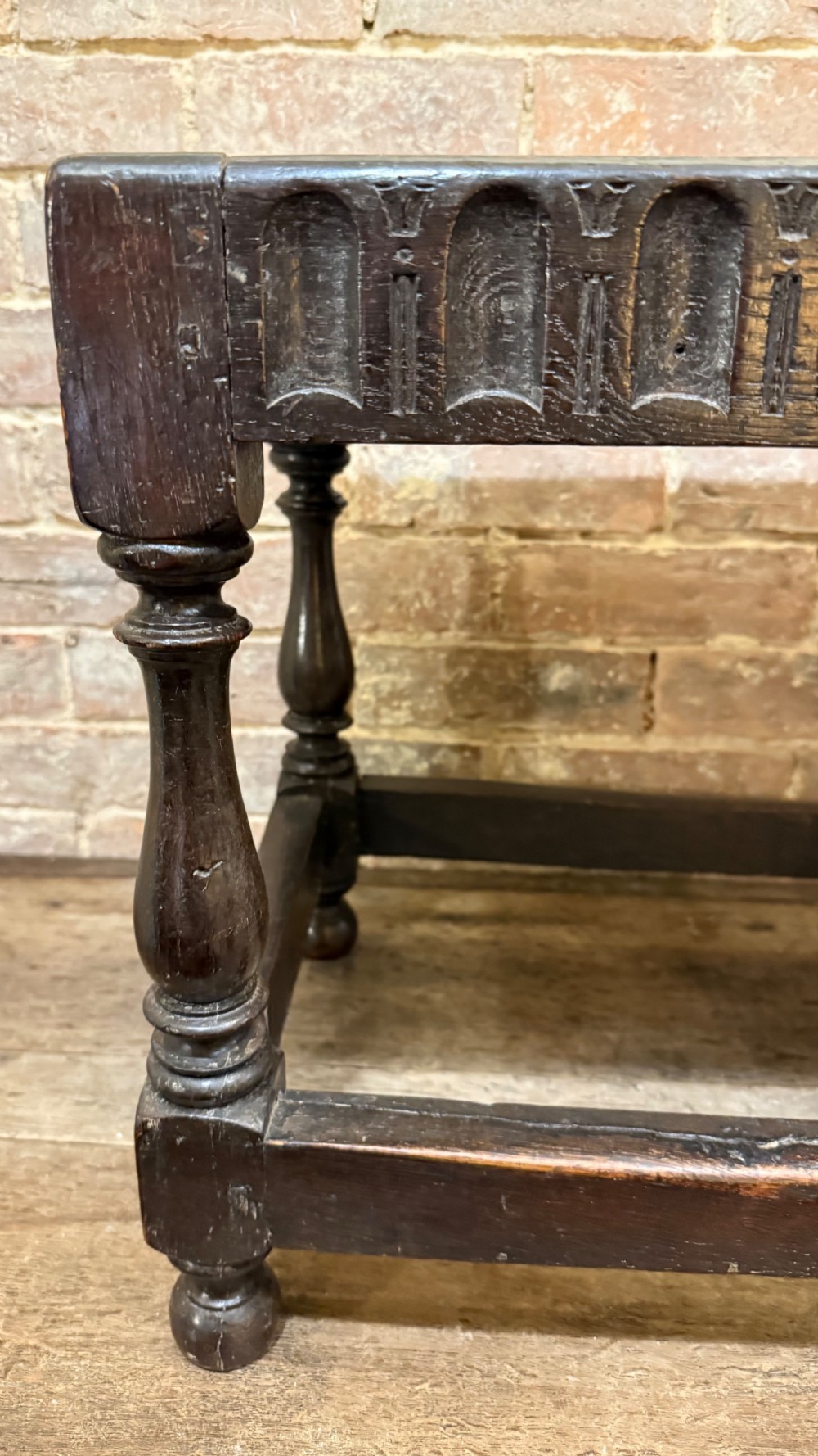 A dark oak 17th-century joint stool featuring a carved arcaded apron, turned legs, and lower box stretchers. View V