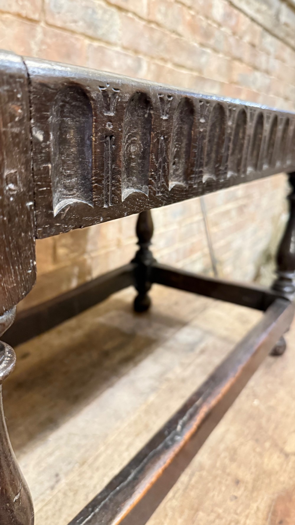 A dark oak 17th-century joint stool featuring a carved arcaded apron, turned legs, and lower box stretchers. View VII