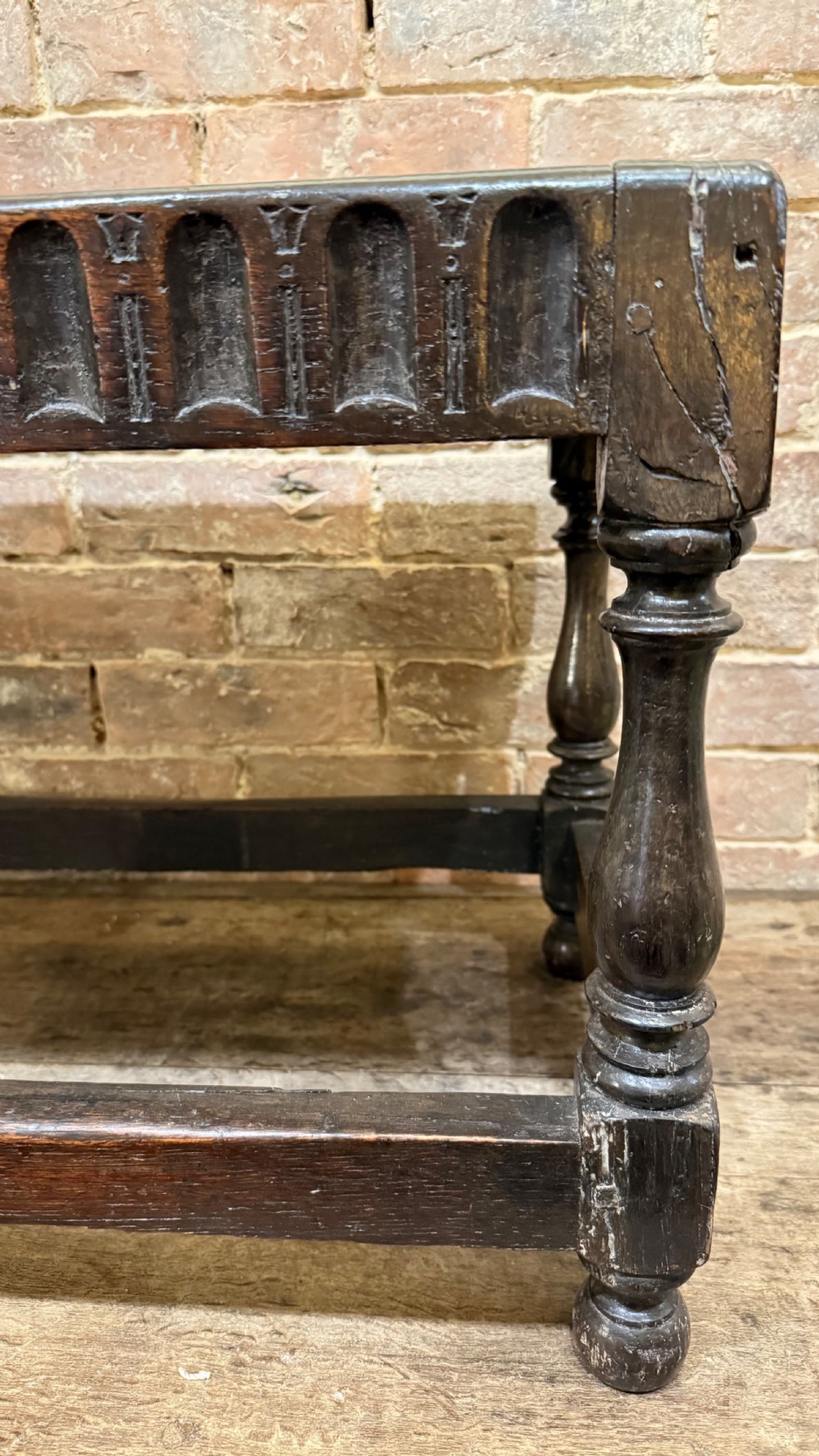 A dark oak 17th-century joint stool featuring a carved arcaded apron, turned legs, and lower box stretchers. View VIII