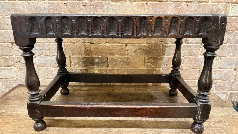 A dark oak 17th-century joint stool featuring a carved arcaded apron, turned legs, and lower box stretchers. View IX