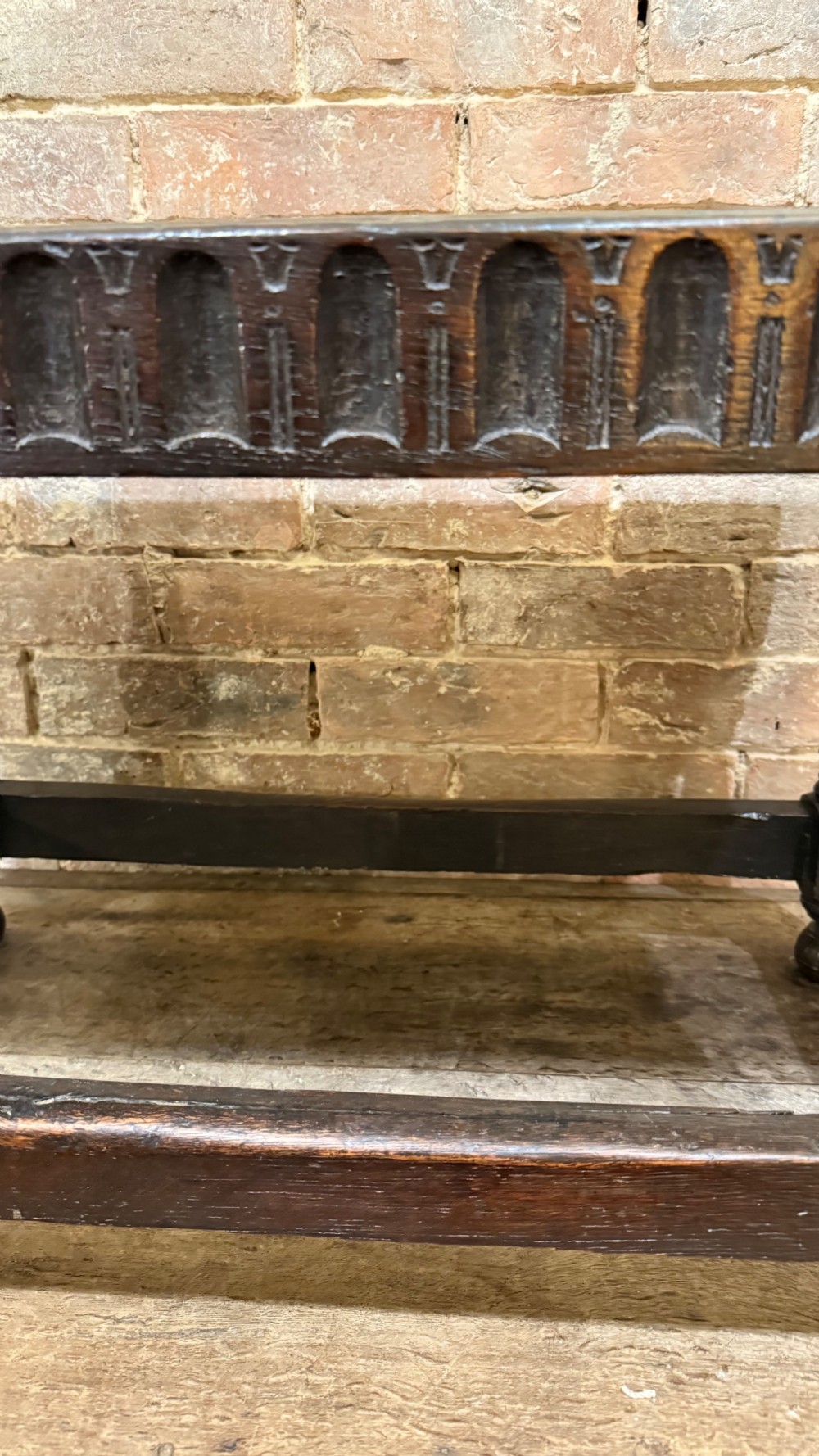 A dark oak 17th-century joint stool featuring a carved arcaded apron, turned legs, and lower box stretchers. View X