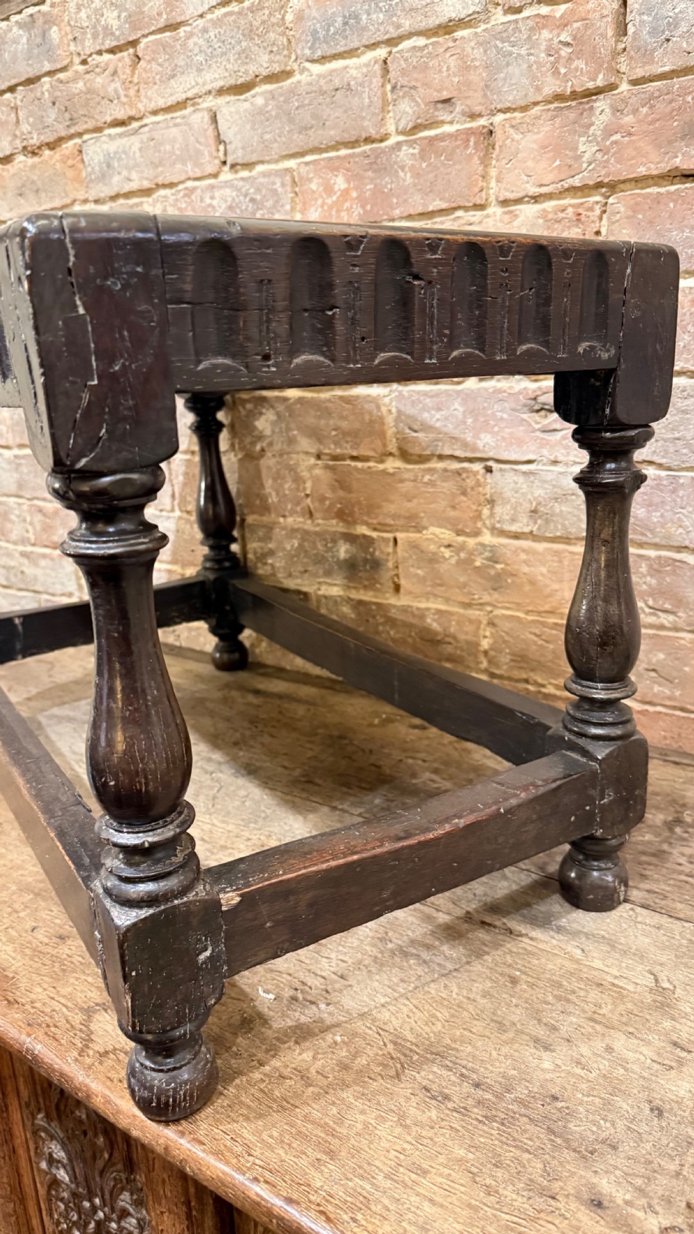A dark oak 17th-century joint stool featuring a carved arcaded apron, turned legs, and lower box stretchers. View XI