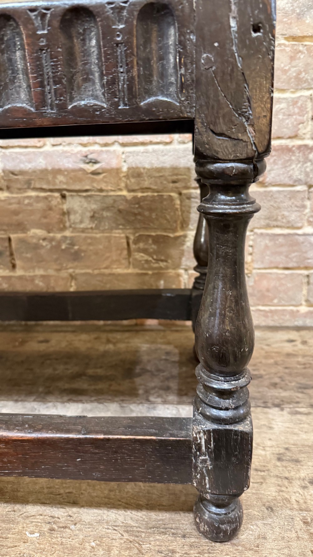 A dark oak 17th-century joint stool featuring a carved arcaded apron, turned legs, and lower box stretchers. View XII