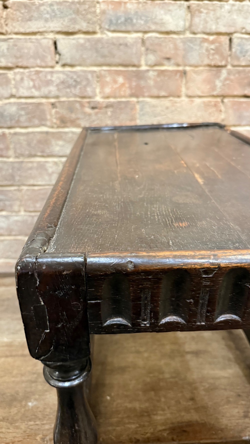 A dark oak 17th-century joint stool featuring a carved arcaded apron, turned legs, and lower box stretchers. View XIII