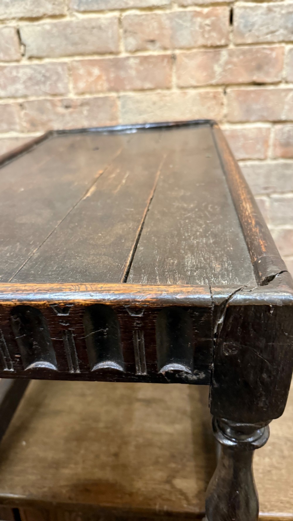 A dark oak 17th-century joint stool featuring a carved arcaded apron, turned legs, and lower box stretchers. View XV