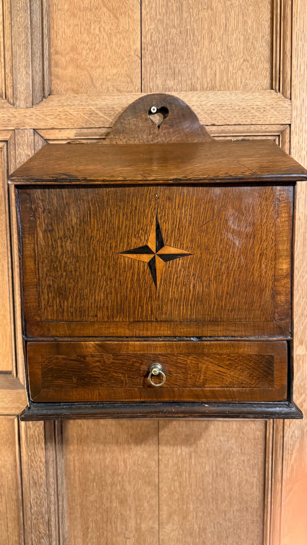 A 19th-century wall-mounted oak box featuring a star marquetry inlay, a heart-shaped hanging cut-out, and a lower drawer with a metal ring pull.