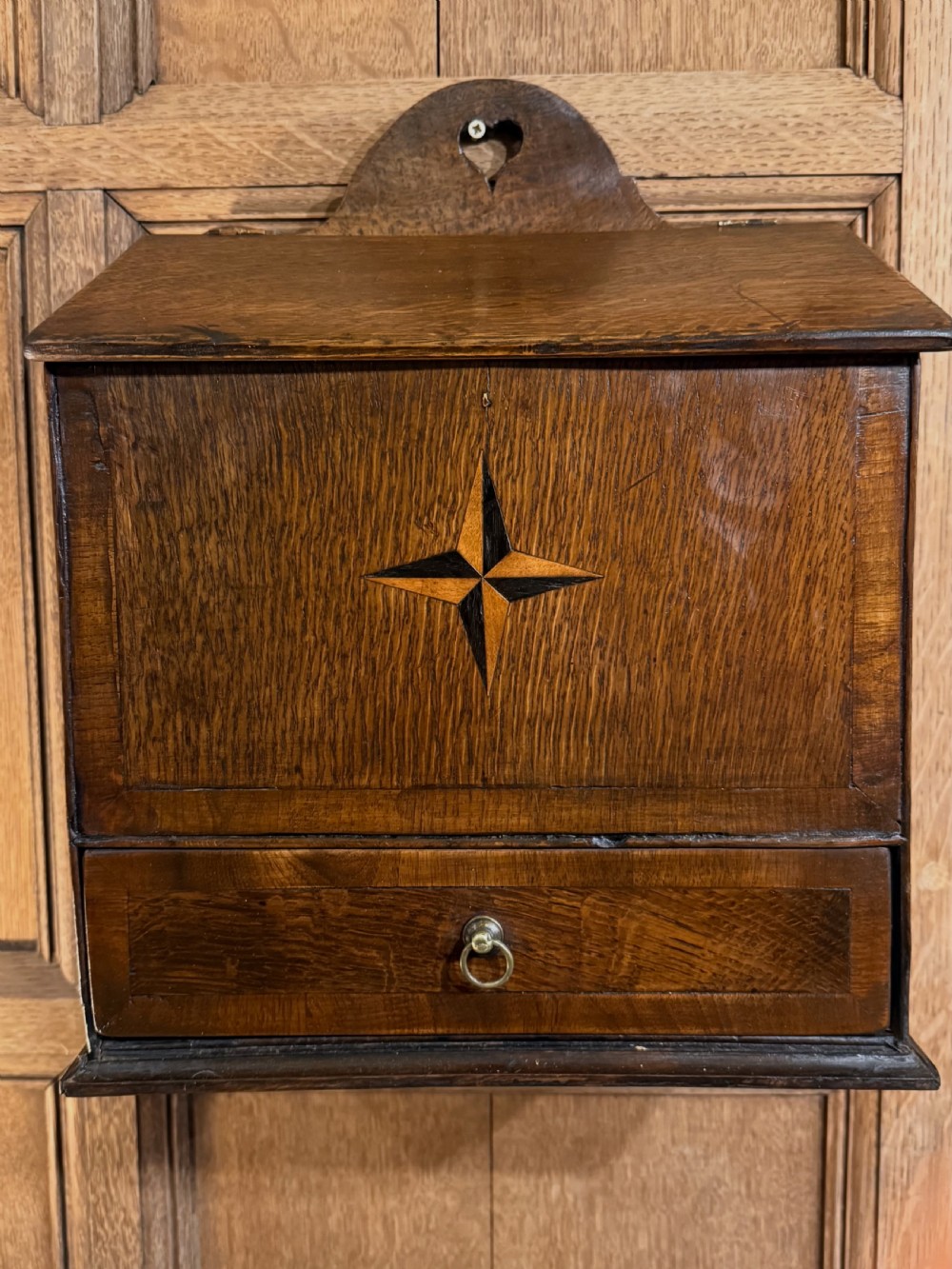A 19th-century wall-mounted oak box featuring a star marquetry inlay, a heart-shaped hanging cut-out, and a lower drawer with a metal ring pull. View V