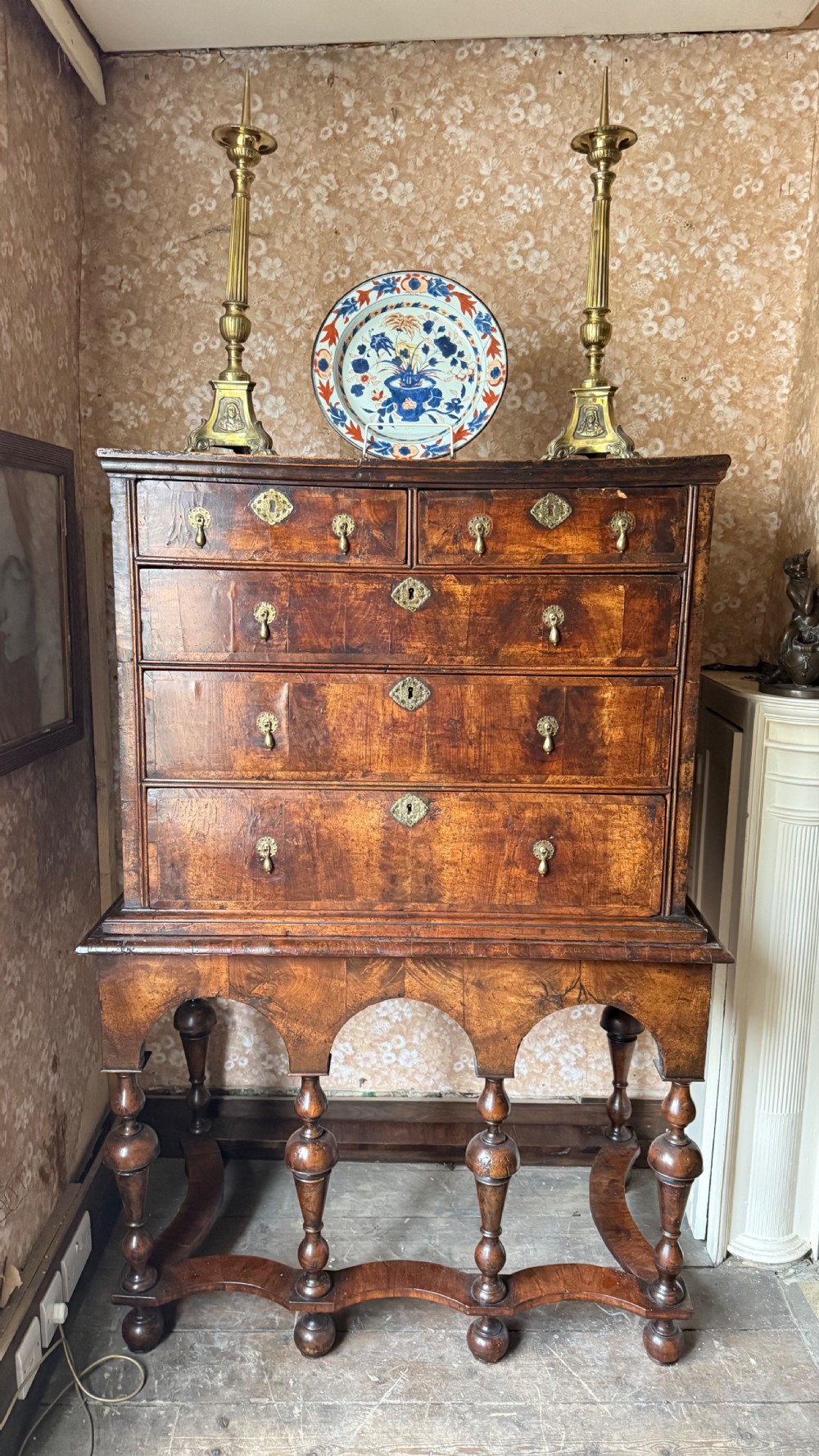 A late 17th-century walnut chest on stand featuring brass drop handles, five drawers, an arched apron, and six turned legs with shaped stretchers.