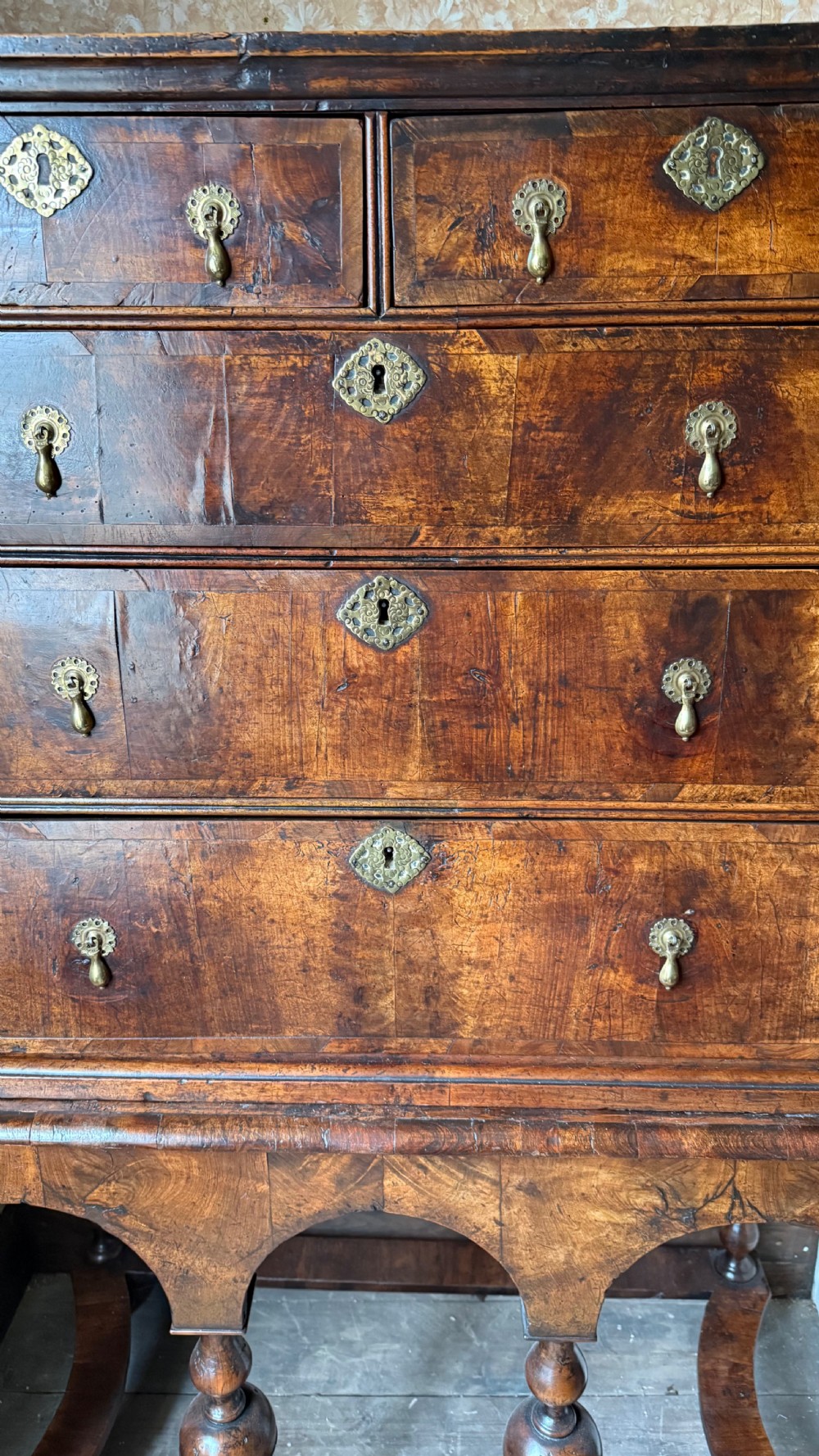 A late 17th-century walnut chest on stand featuring brass drop handles, five drawers, an arched apron, and six turned legs with shaped stretchers. View VI