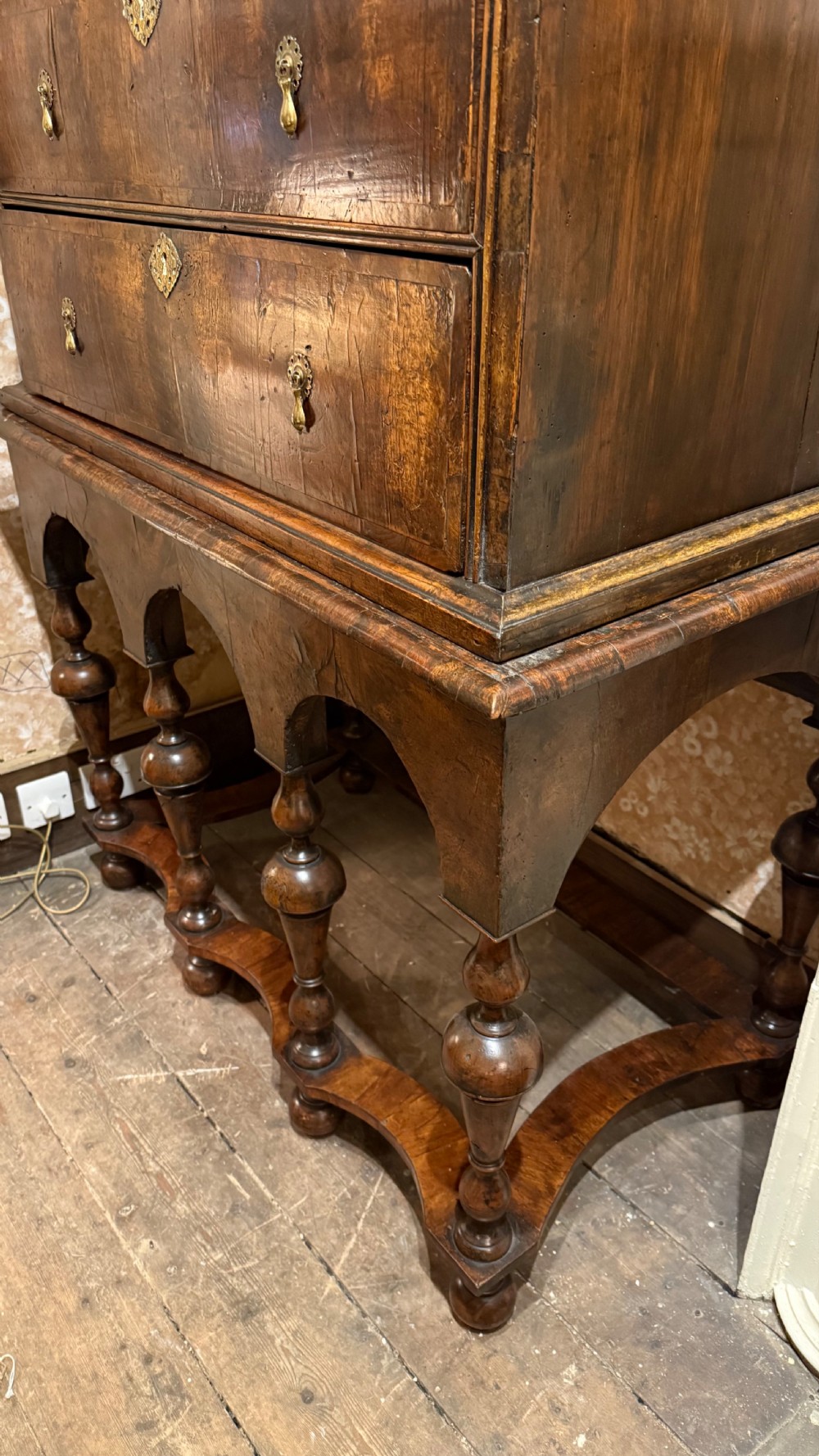 A late 17th-century walnut chest on stand featuring brass drop handles, five drawers, an arched apron, and six turned legs with shaped stretchers. View XIV
