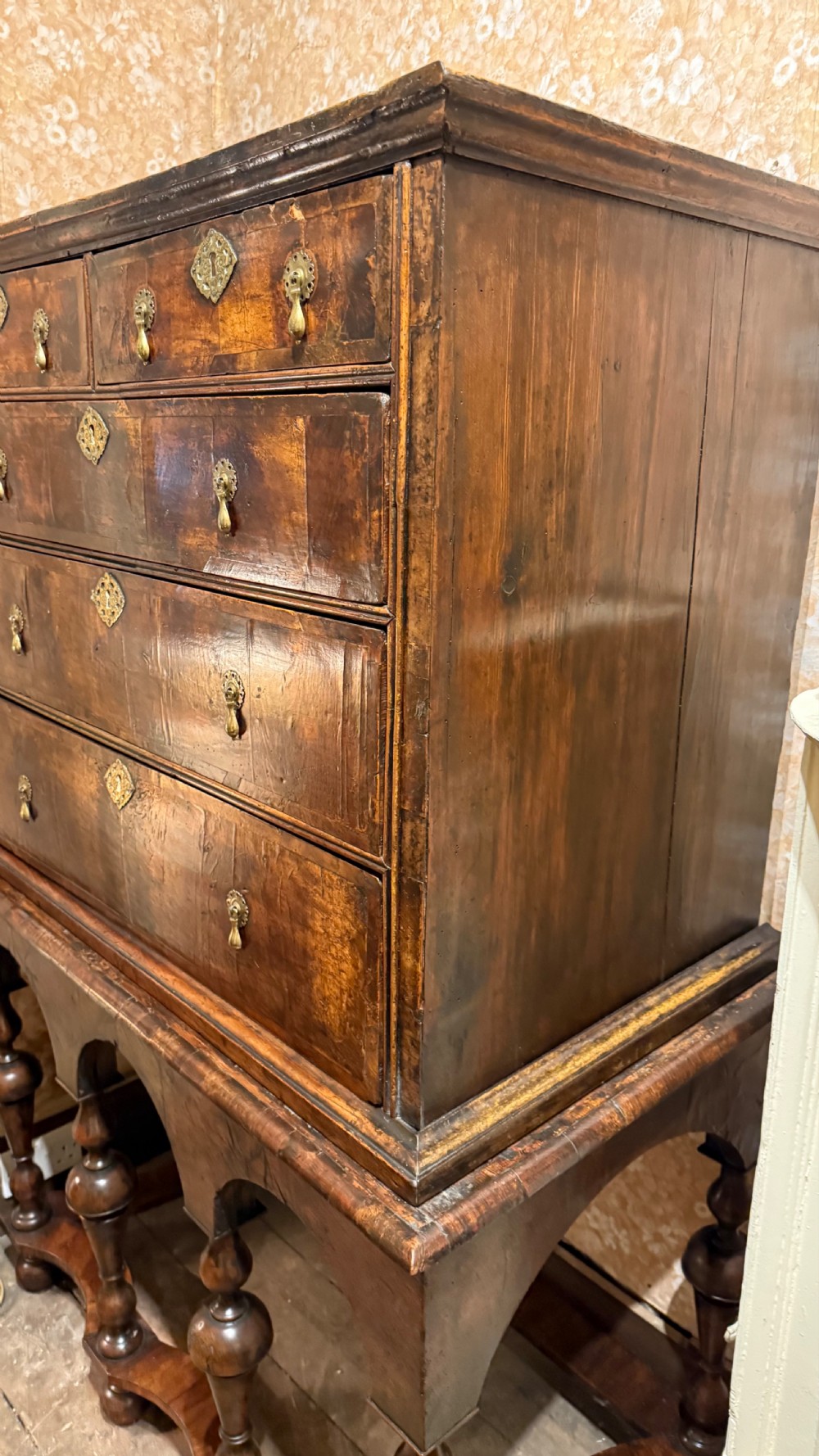 A late 17th-century walnut chest on stand featuring brass drop handles, five drawers, an arched apron, and six turned legs with shaped stretchers. View XV