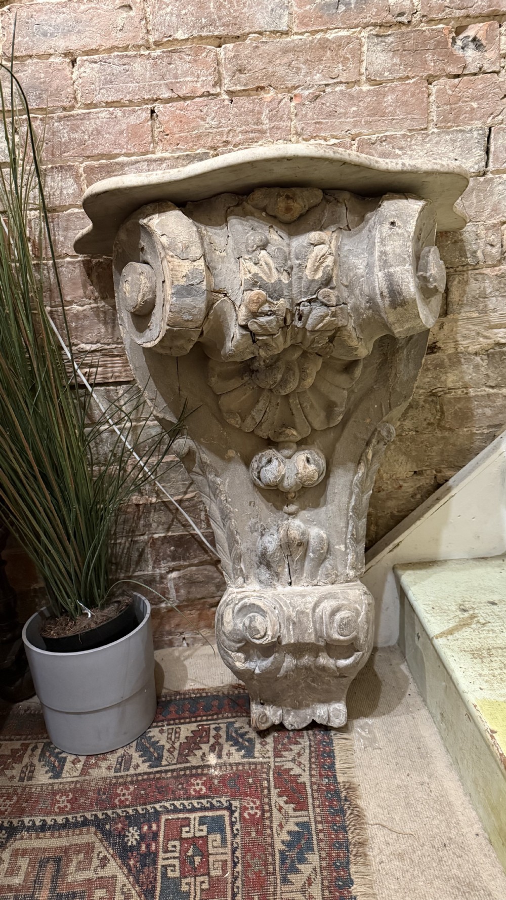 A large hand-carved 18th-century architectural wall bracket featuring scroll volutes, acanthus leaf carvings, and a weathered grey painted finish.