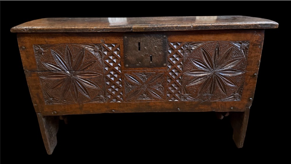 A 16th-century dark oak plank coffer featuring deeply carved floral rosette panels, geometric chip carving, and a central iron lock plate.