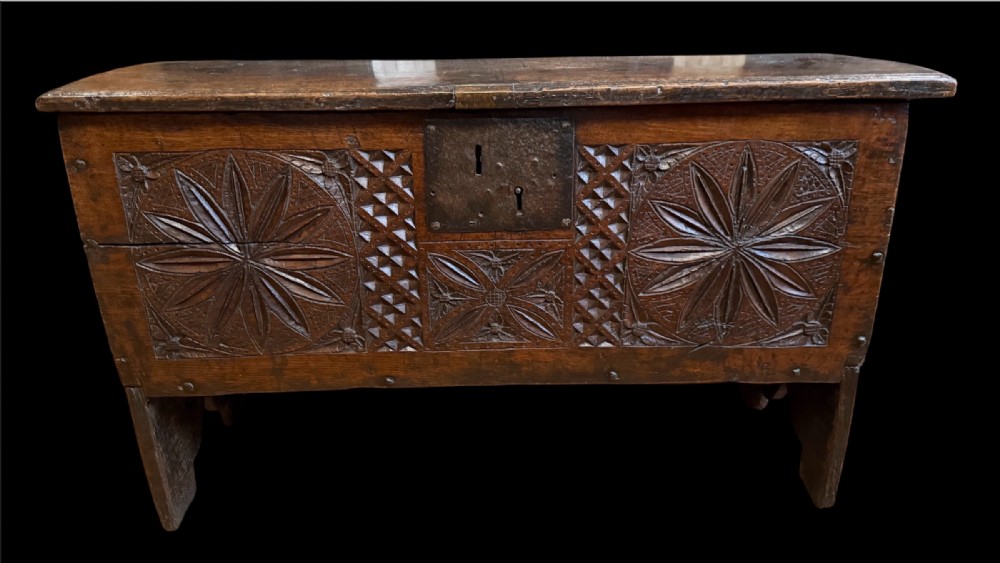 A 16th-century dark oak plank coffer featuring deeply carved floral rosette panels, geometric chip carving, and a central iron lock plate. View III