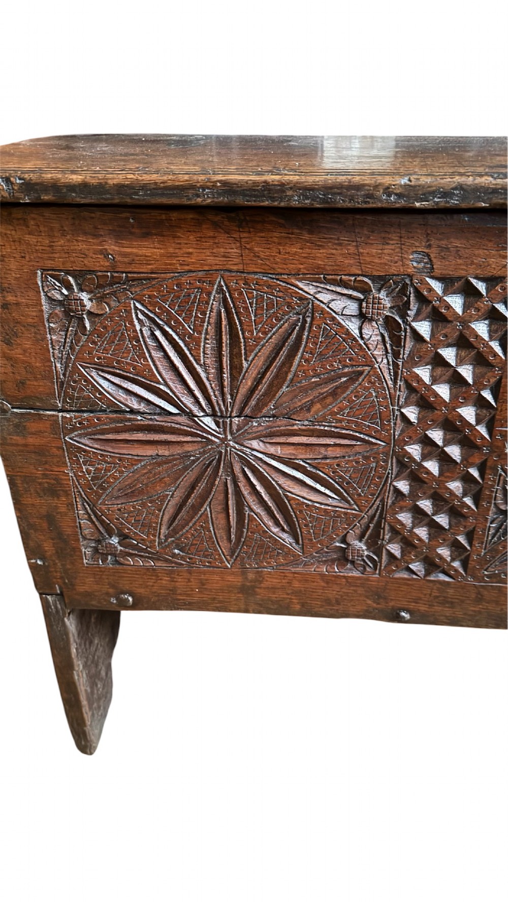 A 16th-century dark oak plank coffer featuring deeply carved floral rosette panels, geometric chip carving, and a central iron lock plate. View V