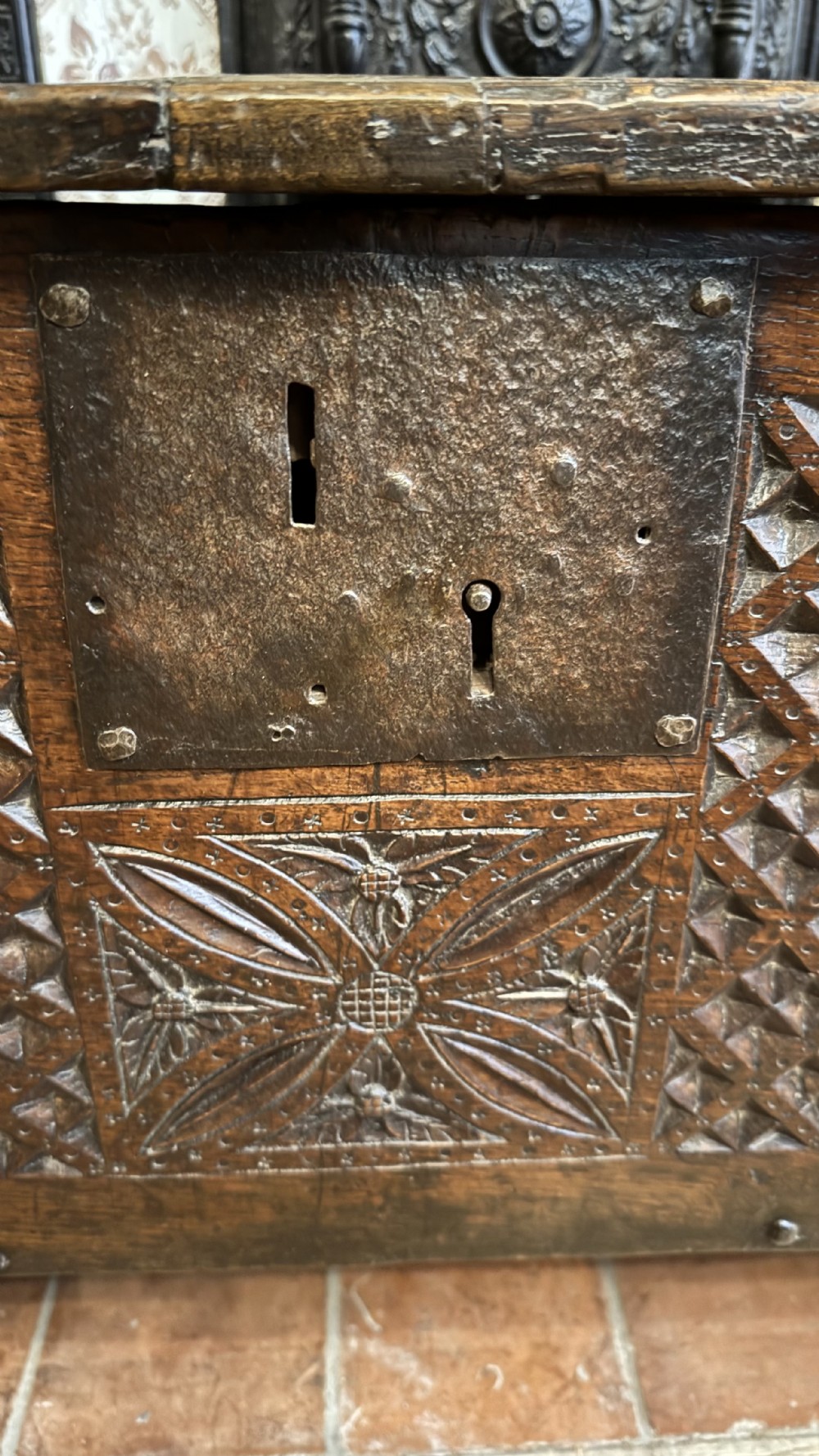 A 16th-century dark oak plank coffer featuring deeply carved floral rosette panels, geometric chip carving, and a central iron lock plate. View VIII