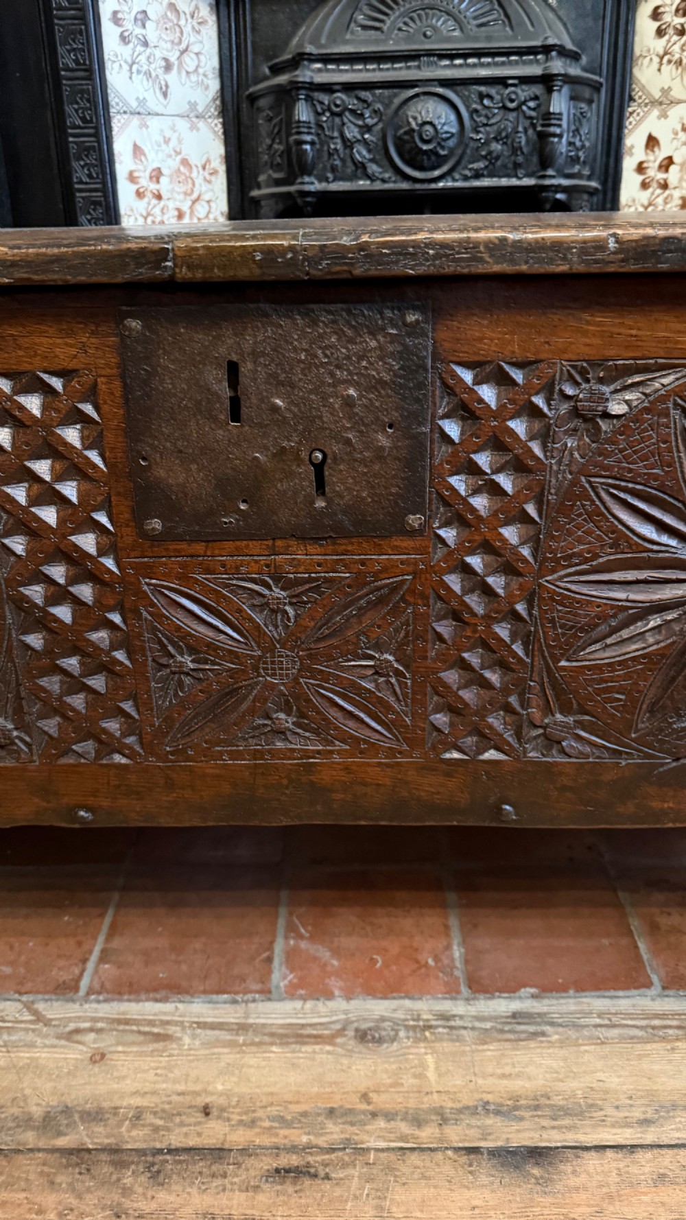 A 16th-century dark oak plank coffer featuring deeply carved floral rosette panels, geometric chip carving, and a central iron lock plate. View XIV