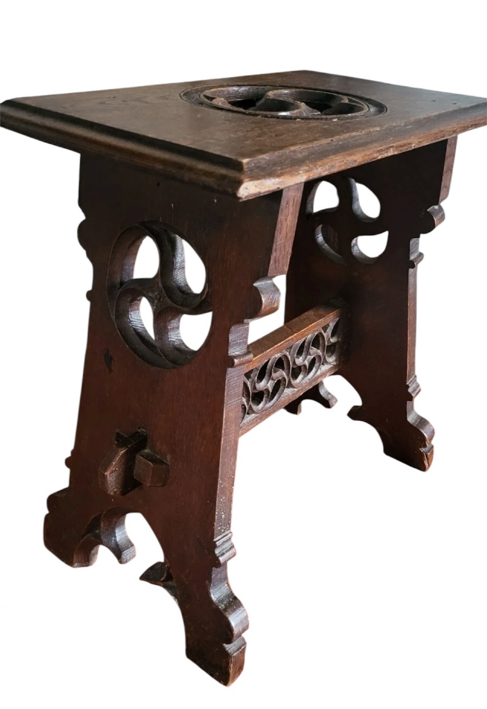 A 19th-century dark oak Gothic Revival stool featuring carved tracery cut-outs on the slab legs, a carved central stretcher, and a carved recessed motif on the top. View III