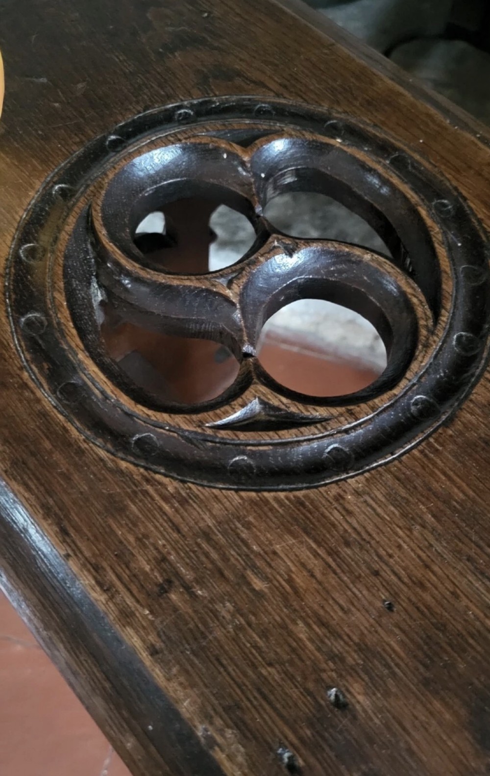A 19th-century dark oak Gothic Revival stool featuring carved tracery cut-outs on the slab legs, a carved central stretcher, and a carved recessed motif on the top. View VII