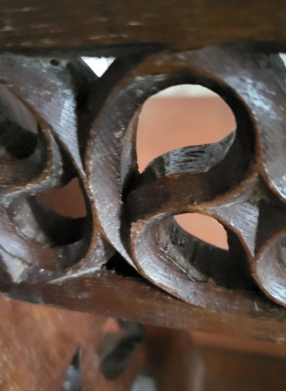 A 19th-century dark oak Gothic Revival stool featuring carved tracery cut-outs on the slab legs, a carved central stretcher, and a carved recessed motif on the top. View X