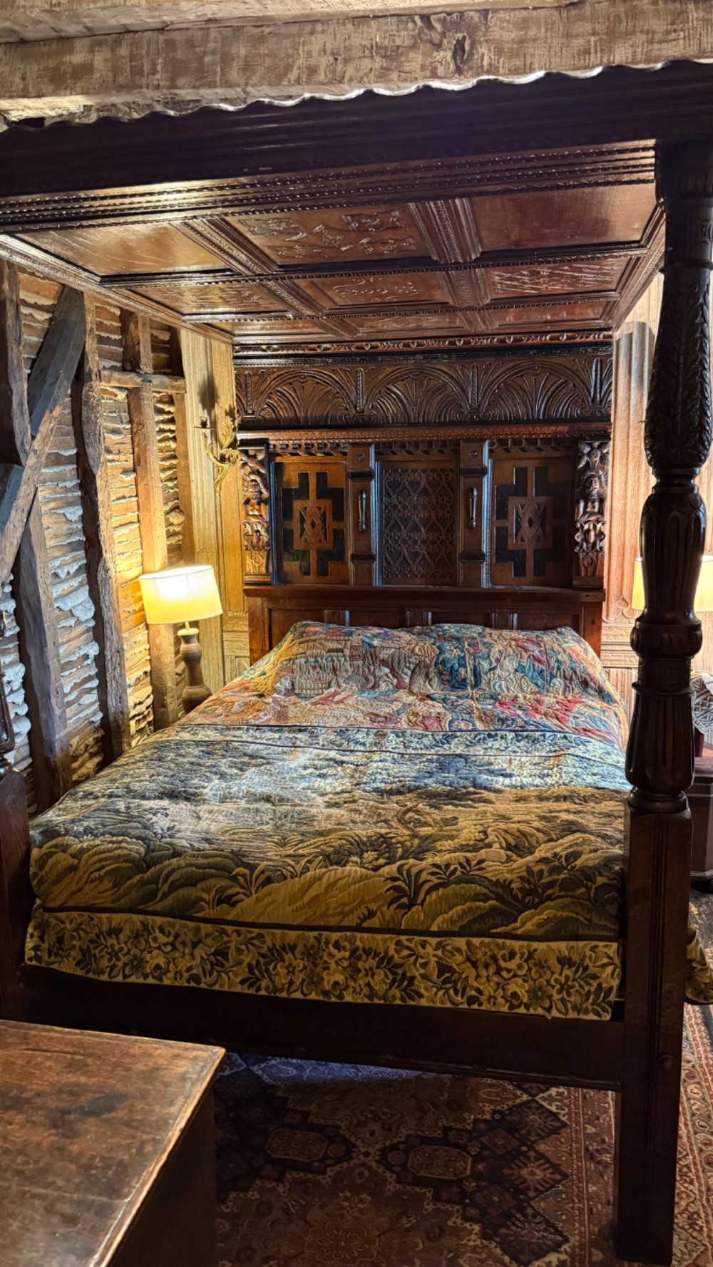 A 17th-century English oak tester bed featuring a heavy panelled canopy, carved geometric headboard, and turned wooden posts.