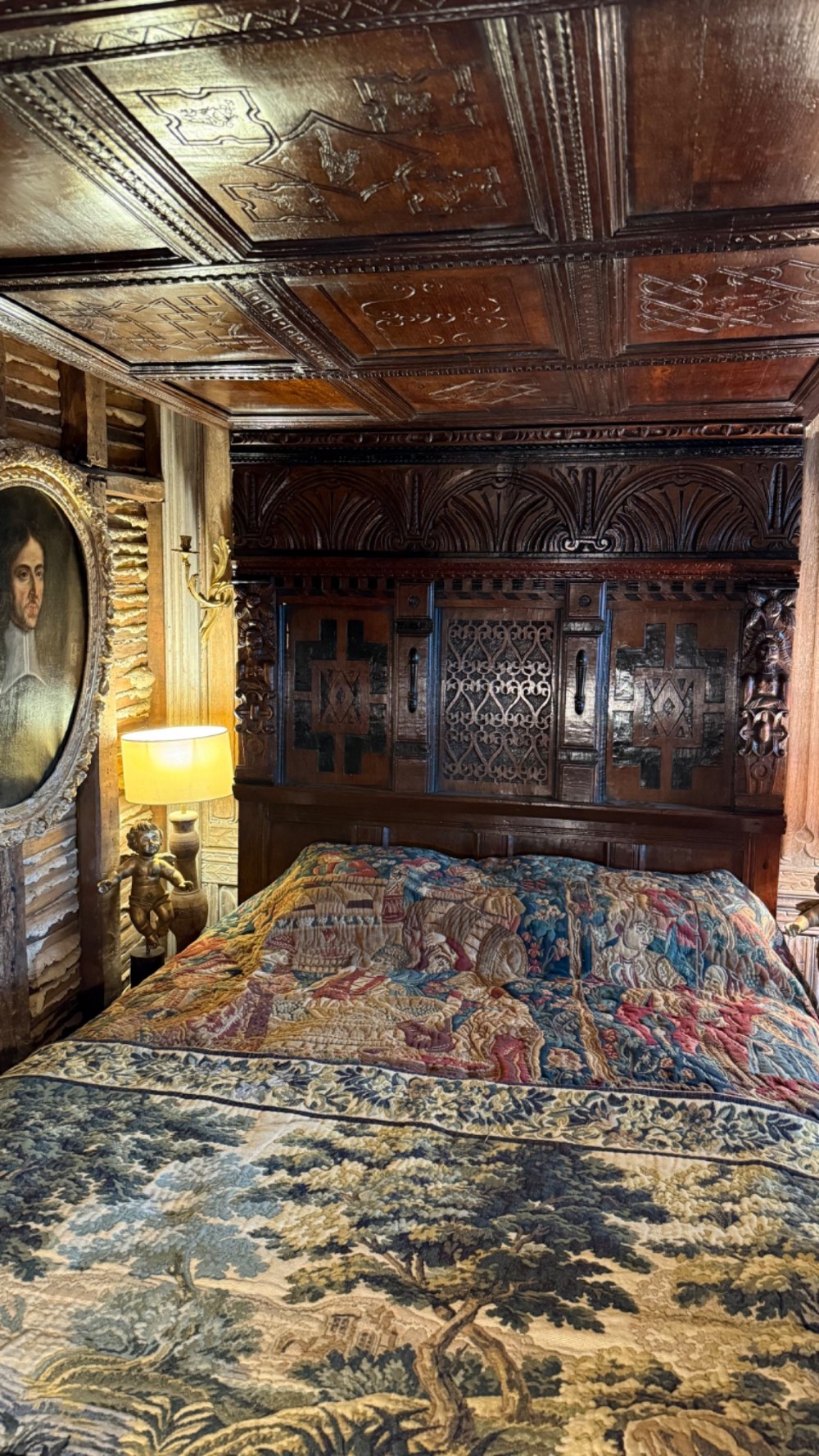 A 17th-century English oak tester bed featuring a heavy panelled canopy, carved geometric headboard, and turned wooden posts. View IV