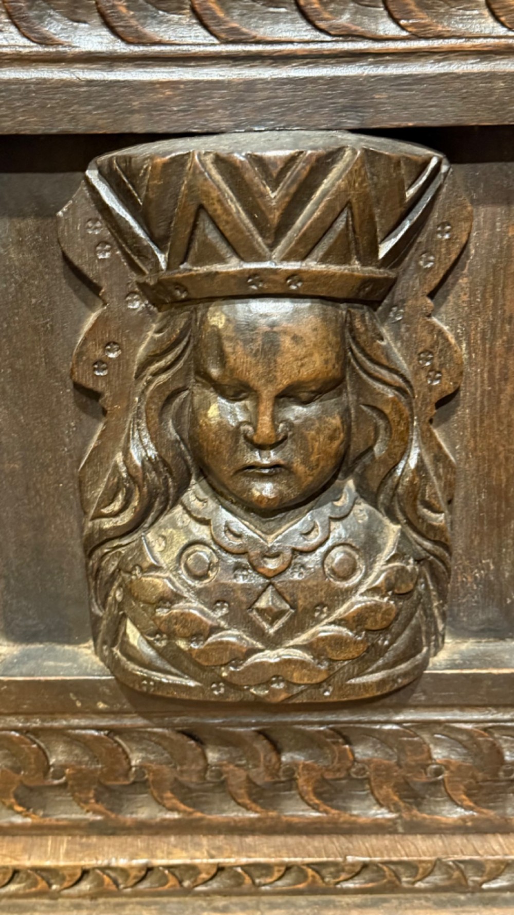 A 17th-century style dark carved oak livery cupboard featuring ornate relief carving, a central face motif panel, turned supports, and an open lower shelf. View V