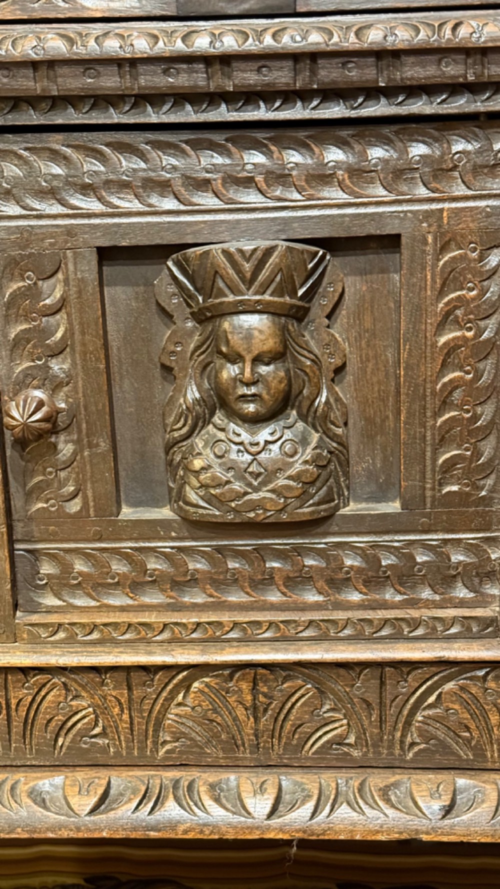 A 17th-century style dark carved oak livery cupboard featuring ornate relief carving, a central face motif panel, turned supports, and an open lower shelf. View VII