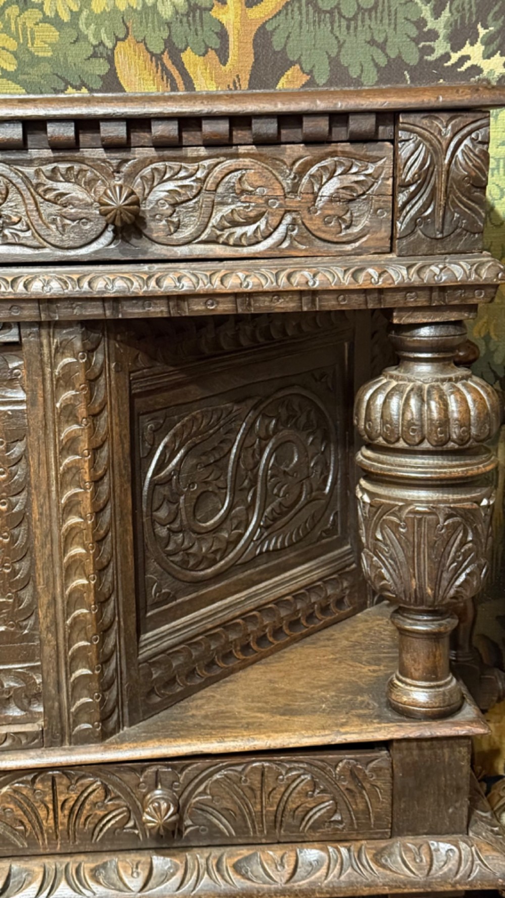 A 17th-century style dark carved oak livery cupboard featuring ornate relief carving, a central face motif panel, turned supports, and an open lower shelf. View VIII